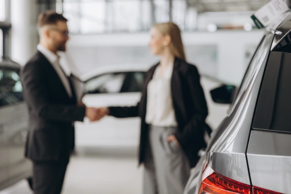 A blurred man and a woman shaking hands beside a caar
